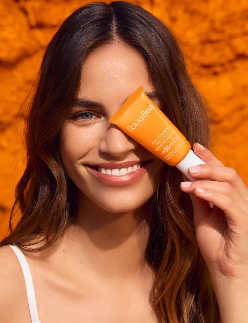 Mujer sonriendo y sosteniendo la crema hidratante C+C Vitamin Dry Touch 50. Producto presentado en nuestros bestsellers.